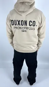 Canguro color tostado con capucha, corte oversize y estampado en la espalda con la leyenda "DUXON CO.", texto en japonés y "TOKYO".