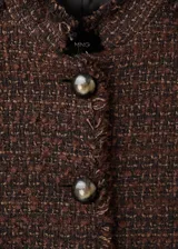 Chaqueta estructurada de tweed en color marrón, de corte recto con cuello redondo, manga larga y cierre frontal de botones. Presenta terminaciones deshilachadas y bolsillos frontales.