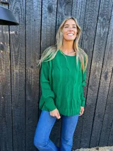 Buzo verde de lana y poliamida, con diseño oversize, cuello redondo y trenzas en la parte delantera.