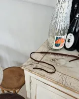 Gargantilla tipo choker de gamuza con dijes colgantes artesanales de metal y perlas naturales. Cuenta con tiras largas para atar y ajustar en la parte posterior.