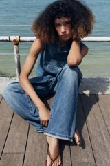 Top de denim blanco sin mangas, con cuello mao y cierre frontal cruzado con trabillas y botones metálicos.