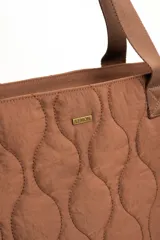 Bolso tipo tote bag color marrón con diseño capitonado de ondas, asas largas y placa metálica con el logo de la marca.