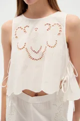 Musculosa de algodón color celeste, con cuello redondo y detalles bordados en tono blanco con diseño de broderie en la parte frontal. Cuenta con cordones laterales para ajustar.