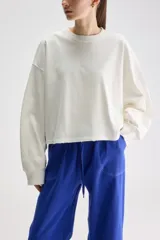 Remera oversize de manga larga y largo cropped color blanco, confeccionada en jersey de algodón, con cuello redondo y terminaciones desgastadas.