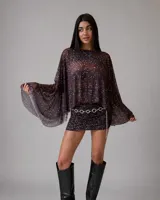 Vestido corto de tul con estampado de puntos blancos sobre fondo negro, compuesto por una capa superior holgada de mangas amplias y una falda ajustada con frunces laterales.