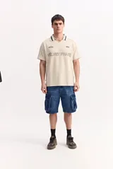 Remera polo beige con textura, cuello en V con solapa y detalles en contraste, de manga corta y diseño urbano con estampas frontales.