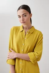 Vestido camisero midi color mostaza, de lino, con cuello camisero, mangas 3/4 con trabillas y cierre frontal con botones.