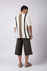 Remera de punto con textura piqué, manga corta y cuello redondo. Presenta un diseño de rayas verticales en tonos crudo, marrón y negro.