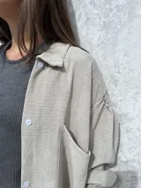 Camisa oversize de textura ligera y efecto nevado, con cuello clásico, cierre frontal de botones y mangas largas con detalle de frunces en los hombros.