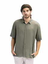 Camisa de manga corta color verde oliva, confeccionada en lino y viscosa, con cuello clásico y cierre frontal con botones. Corte suelto y estilo casual.