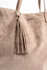 Bolso tipo tote de gran tamaño confeccionado en gamuza sintética color tostado. Presenta un diseño minimalista con asas largas de hombro y una pequeña placa metálica frontal con el logo de la marca.