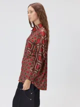 Camisa de seda con cuello camisero, manga larga y bolsillo frontal. Presenta un diseño estampado geométrico de cuadrados en tonos marrones y azul oscuro.