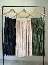Maxi falda color beige con flecos escalonados y diseño de capas, confeccionada en tela elastizada con cintura elástica.