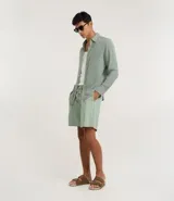 Bermuda recta de playa en color blanco roto, confeccionada en algodón texturizado con efecto de rayas verticales. Posee cintura elástica con cordón ajustable.