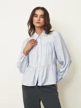 Camisa de corte amplio y estilo romántico, color celeste, con cuello clásico, cierre frontal de botones y diseño de canesú fruncido. Presenta mangas largas abullonadas con puños elásticos.