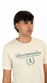 Remera de algodón color crema con cuello redondo y mangas cortas. Presenta un estampado frontal en color verde con el logo de la marca Duxon Studios y un diseño de corona de laureles.
