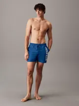 Short de baño de largo medio Calvin Klein, confeccionado en poliéster reciclado de secado rápido. Presenta cintura elástica con cordón ajustable, forro de malla interior, bolsillos laterales y un bolsillo trasero. Destaca por el logo de la marca estampado en vertical sobre la pierna.
