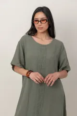 Vestido midi de lino color beige, con mangas cortas, cuello redondo, alforzas verticales en el pecho y detalle de volados en el ruedo.