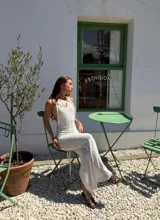 Vestido largo blanco de tejido texturizado, con escote halter anudado y aberturas laterales pronunciadas en la cadera.