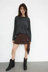 Falda pantalón de tiro bajo en color negro, con cintura drapeada y detalle de tira lateral colgante. Presenta un diseño con volantes en el bajo y cierre de cremallera metálica.