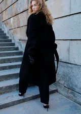 Abrigo largo de lana italiana Manteco en color negro, con diseño recto y cuello de pelo sintético desmontable. Presenta solapas con muesca, cierre con cinturón tipo batín, dos bolsillos laterales y forro interior.
