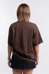 Remera de corte holgado color marrón chocolate, con cuello redondo y mangas cortas. Presenta un estampado frontal en color rojo con un diseño de elipse y una estrella.