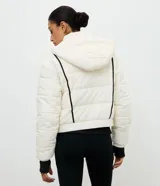 Campera puffer deportiva Get Over, color blanco con detalles de bies en color negro a lo largo de las mangas. Presenta cuello alto con capucha integrada, cierre frontal con botones a presión, bolsillos laterales con cremallera y puños con elásticos.