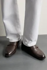 Zapato de vestir tipo monk de color negro, con detalle de doble hebilla metálica plateada en el empeine, puntera redondeada y suela con ligero tacón.