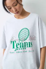 Remera de algodón gris melange con corte oversize, manga corta y estampa localizada en el frente con motivos deportivos en tonos verde y rosado.