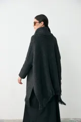 Poncho de tejido artesanal en color negro, con cuello alto tipo polera, mangas largas y terminación con flecos en el ruedo. Presenta una etiqueta de cuero decorativa en la parte inferior.