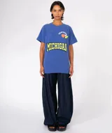 Remera de algodón gris oscuro con lavado especial, corte holgado y cuello redondo. Presenta un estampado frontal con la palabra "MICHIGAN" en amarillo neón con borde negro, y apliques decorativos en la parte superior: un corazón naranja, la palabra "NEWTONE" en arco y dos píldoras/pastillas de colores.