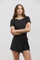 Vestido deportivo corto de color negro, diseñado para pádel. Presenta una estructura superior tipo remera de manga corta con espalda abierta, y una parte inferior que combina una calza corta con una media pollera envolvente que se ata en la cintura. Confeccionado en tejido suave y elástico.