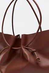 Bolso tipo tote bag negro de cuero sintético, con frunce superior ajustable con cordones y doble asa de hombro.