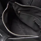 Cartera tipo tote de cuero sintético color negro, con doble asa de hombro, cierre superior y placa metálica decorativa con logo en el frente.