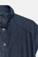 Chaleco de denim azul oscuro con cuello alto, manga sisa y cintura ajustable con elástico. Cierre frontal con botones a presión metálicos.