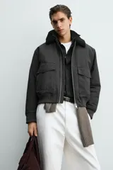 Cazadora bomber de corte cropped confeccionada en algodón, color negro. Presenta cuello de solapa con efecto borreguillo a contraste, cierre frontal con cremallera metálica, bolsillos delanteros tipo plastrón con solapa y acabados en rib en puños y bajo.