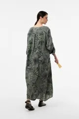 Vestido largo de lino de calce relajado y silueta fluida, con estampa botánica en tonos verdes y azules sobre fondo beige. Cuenta con escote en V y mangas amplias.