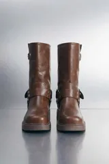 Botas de caña media color marrón, elaboradas en cuero vegano, con diseño estilo biker, taco bajo, hebillas metálicas decorativas y argollas laterales.