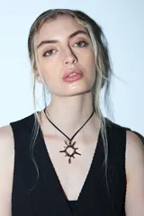 Collar de cordón negro con dije metálico en forma de sol con diseño irregular y puntas alargadas.