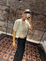 Blusa de tejido transparente color negro con diseño texturizado de mini flores en relieve, de mangas cortas y corte holgado.