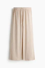 Pantalón amplio de punto, tiro alto, con cintura elástica y cordón ajustable. Presenta un diseño de rayas verticales en tonos beige y marrón claro.