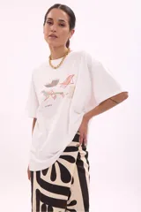 Remera oversize blanca de manga corta, con cuello redondo y estampa frontal ilustrada con reposeras y la inscripción "La Siesta".