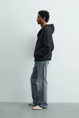 Sudadera tipo hoodie de corte relajado, confeccionada en tejido de algodón con textura estructurada y efecto lavado. Presenta cierre frontal con cremallera, cuello con capucha, manga larga, bolsillos tipo canguro y acabados en rib.