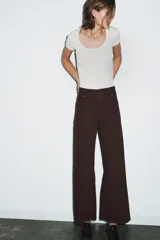 Jeans de tiro alto confeccionados en mezcla de algodón, con diseño de pierna ancha y costura marcada en el delantero. Presenta cintura con trabillas, cierre frontal con cremallera, botón y gancho metálico, y bolsillos de plastrón en la espalda.