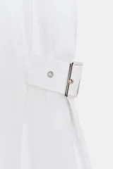 Vestido midi blanco, sin mangas, con cuello solapa y escote pico. Presenta falsos bolsillos con solapas en el pecho, trabillas con hebillas en la cintura y cierre frontal de botones.