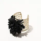 Brazalete dorado con diseño calado y aplique de flor negra.