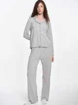 Camisa de pijama de manga larga con cuello solapa y cierre frontal de botones. Presenta un estampado sutil de pequeños corazones sobre una base de color gris melange, con detalles de ribete en contraste en el cuello y la botonera.