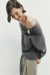 Jersey de punto color gris oscuro, con escote recto tipo off-shoulder, manga larga y detalle de aplique metálico en el hombro. Presenta acabados en rib en puños y ruedo.