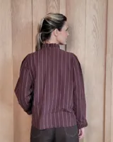 Camisa de algodón a rayas verticales blancas y azules, con cuello alto tipo gorguera con volados, cierre frontal de botones y mangas largas con puños con volados.