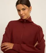 Campera deportiva color bordó confeccionada en microfibra pesada, con cuello alto doblado, puños ajustados y cremallera delantera con cordón en el tirador.